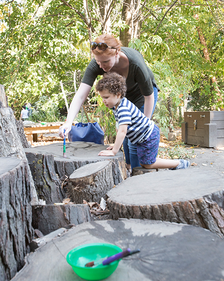 A zoo educator and a child play on tree stumps